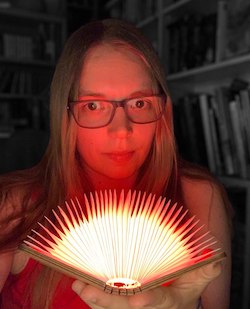 Profilfoto: weiße, blonde Frau mit Brille und leuchtendem Buch